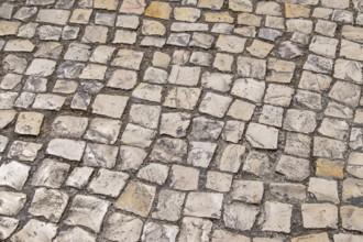 Irregular paving stones in shades of beige and gray create an antique street texture, Portugal
