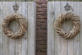 Two decorative wreaths made of branches hang symmetrically on a rustic wooden board in front of a