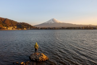 Young man standing on rocks in Lake Kawaguchi, view of Mount Fuji volcano at sunset, Yamanashi