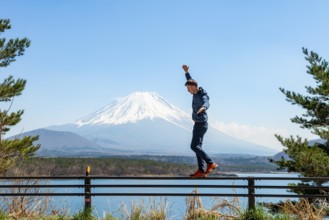 Young man balancing on railings next to a road, view across the lake to Mt Fuji volcano, Motosu