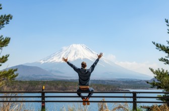 Young man sitting on railings next to a road and stretching his arms in the air, looking across the