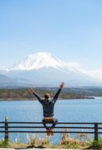 Young man sitting on railings next to a road and stretching his arms in the air, looking across the