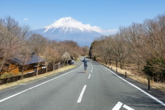Young man jumping on road, road leading to Mount Fuji volcano, wanderlust, Yamanashi Prefecture,