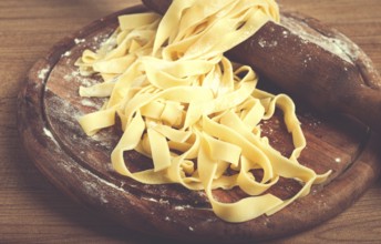 Raw tagliatelle pasta, homemade, on a rolling pin, top view, on a cutting board, cooking concept