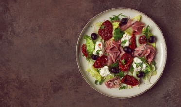 Salad with dried tomatoes, prosciutto, soft cheese, olives, homemade, top view