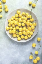 Yellow cherry, cherry berry, scattered on a plate, top view, no people