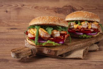 Two shrimp burgers and buns with sesame seeds, bacon, lettuce, tomatoes and onions, on a wooden
