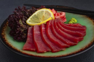 Fresh tuna sashimi served with lemon, wasabi, and pickled ginger on a dark background