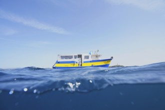 A yellow-blue boat, motor ship, dive boat floats on the calm sea under a clear sky on the