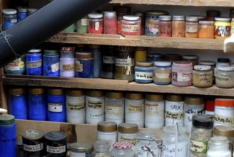 Glasses with various color powders and pigments on a wooden shelf, artist workshop, Zurich,