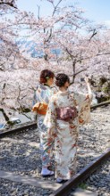 Keage Incline, two Japanese women wearing kimonos taking selfies on old tracks, cherry trees