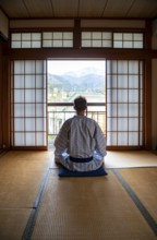 Young man wearing kimono sitting in traditional Japanese living room with tatami mats and shoji