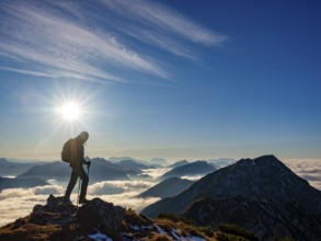 Mountaineer looking at blue-colored silhouette of mountains, fog in the valley, Hochstaufen,