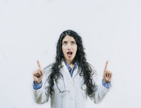 Young female doctor looking and pointing promotion up isolated. Surprised female doctor pointing up