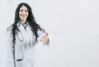 Latin female doctor shaking hands at the camera gesturing welcome. Smiling female doctor gesturing