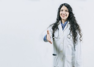 Smiling female doctor gesturing welcome, isolated. Latin female doctor shaking hands at the camera