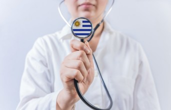 Female doctor holding stethoscope with Uruguay flag. National health system of Uruguay