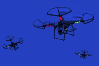 Three illuminated miniature quadcopter drones, teleoperated unmanned aerial vehicles, UAV equipped