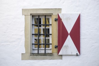 Window with red and white shutters and iron bars in front of a white wall, Münsterland, North