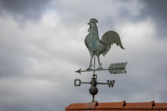 Rooster weather vane on a tiled roof against a dark cloudy sky, Baden-Württemberg, Germany