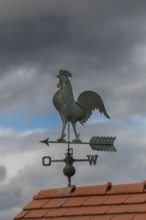 Metallic weather vane on a tiled roof, dramatic sky in the background, Baden-Württemberg, Germany