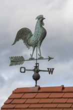 Rooster on metal weather vane on a tiled roof, clouds in the background, Baden-Württemberg, Germany