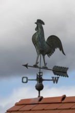 Metal weather vane with rooster on a tiled roof, blue sky and clouds, Baden-Württemberg, Germany