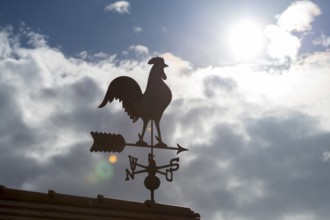 Silhouetted weather vane against cloudy sky with bright sun, Baden-Württemberg, Germany