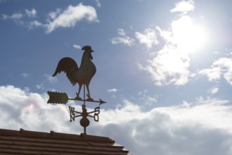 A weather vane on a roof in sunshine against a cloudy sky, Baden-Württemberg, Germany