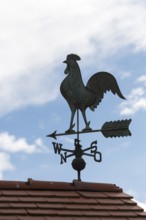 A dark weather vane on a roof against a blue sky with clouds, Baden-Württemberg, Germany