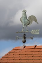 Metal weather vane with rooster on a tiled roof against a blue sky, Baden-Württemberg, Germany