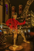 Schäffler dancers made of wire and string of lights, in the back the towers of the Church of Our