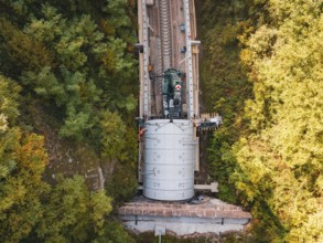 Crane photographed from the air above a tunnel opening in an autumnal landscape, building of