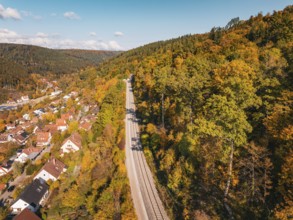 Village next to railroad tracks in autumn landscape with hills and forest, building of Hermann,