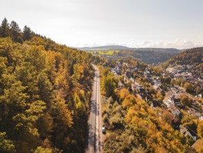 Autumn landscape with railway line through forest and village in hilly surroundings, building of