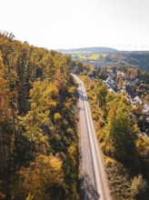 Railway tracks run through autumn landscape and forest next to a village, aerial view, Hermann