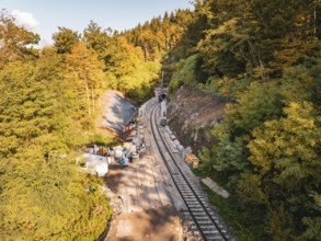 Construction work on railway tracks in an autumnal forest in sunny weather with machines,