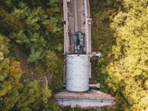 Bird's eye view shows crane over tunnel on a railway line surrounded by trees, construction of