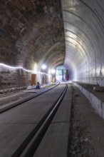 Tunnel with rails and illuminated exit, various materials visible, construction of Hermann, Hesse,