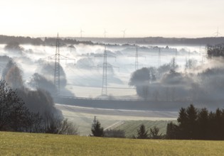 Landscape view with power poles and wind turbines in foggy morning light, Swabian Alps,