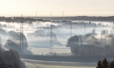 Foggy landscape with power poles and distant wind turbines in the morning, Swabian Jura,