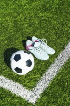 Soccer ball on artificial green turf beside light blue cleats and white boundary line, close top