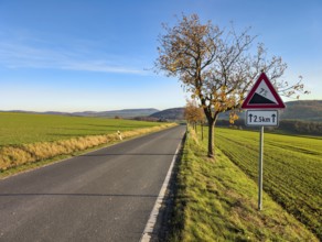 Country road through hilly, agricultural landscape, road sign warns of slopes, slopes, sunny autumn