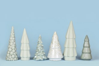 Row of different shaped light green ceramic Christmas trees on blue background