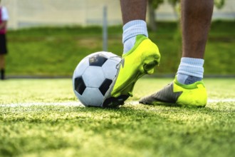 Soccer player foot in neon green cleats controlling a black and white ball on synthetic turf in