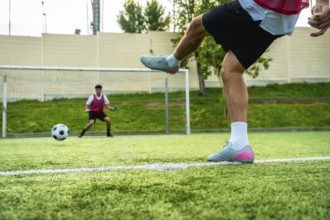 Soccer player's leg striking a football during a penalty kick on a green artificial turf field,