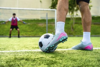 Soccer player's foot rests on a football, ready to take a penalty shot on a green artificial turf