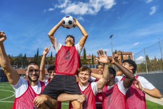 Young male soccer team members celebrating a goal or game victory on a green athletic field,