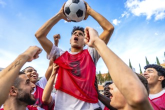 Young diverse men's soccer team members are cheering loud with fists raised and one player is