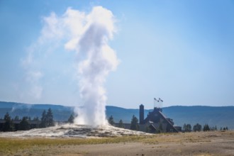 Majestic old faithful geyser erupting with old faithful lodge behind in yellowstone national park